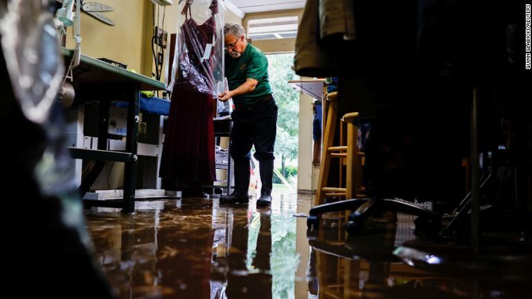 洋服店の店主が浸水で被害を受けた服にカバーをかける＝１日/Quinn Glabicki/Reuters