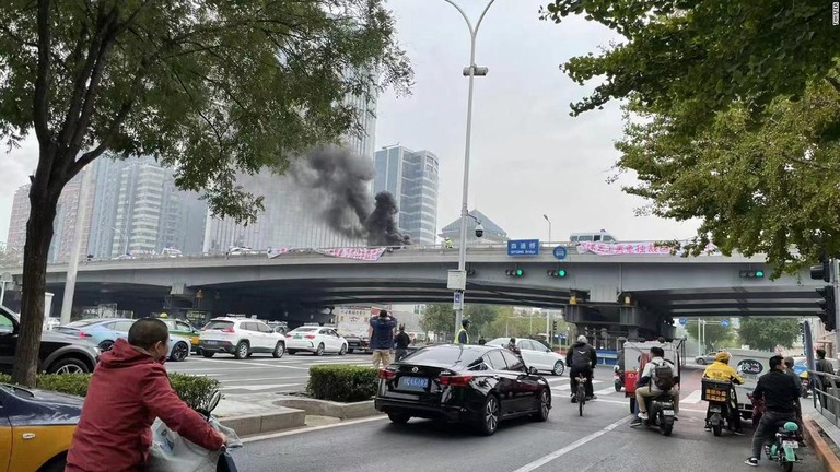 陸橋に掲げられた抗議の横断幕と立ち上る煙＝１３日、中国・北京/Twitter