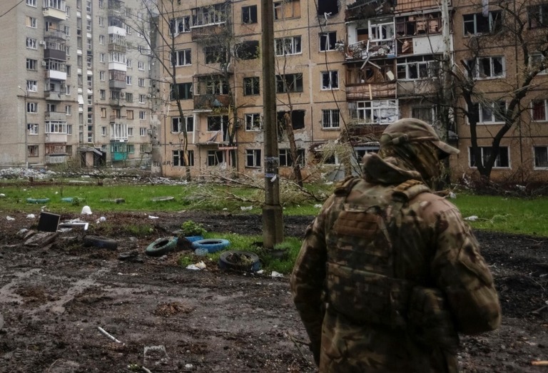 ロシアの攻撃で損傷した住宅のそばを歩くウクライナ軍要員/Anna Kudriavtseva/Reuters