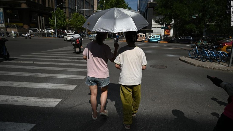 熱波の中、日傘で日差しを避けながら道路を渡る中国・北京の住民/Greg Baker/AFP/Getty Images