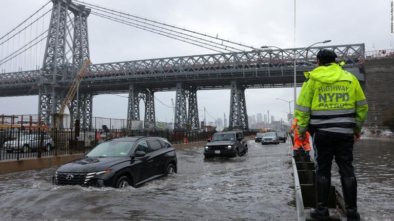 大雨で冠水した道路を走行する車両を見守るニューヨーク市警の警官/Andrew Kelly/Reuters