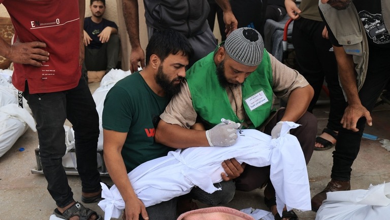 ガザ地区の病院でイスラエルの爆撃により死亡した子どもを包む布に故人の名を書く男性/Mahmud Hams/AFP/Getty Images