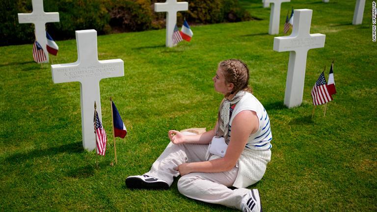 米国の墓地で十字架のそばに座る女性＝６日、コルビルシュルメール付近/Laurent Cipriani/AP