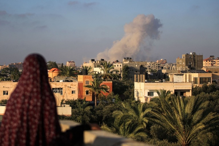 イスラエル軍の攻撃を受けて煙が立ち上る町を見守るパレスチナの女性＝１１日、パレスチナ自治区ガザ地区ガザ市南部/Eyad Baba/AFP/Getty Images