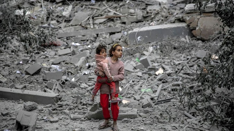 がれきの中を子どもを抱いて移動する少女＝３月、パレスチナ自治区ガザ地区/AFP/Getty Images