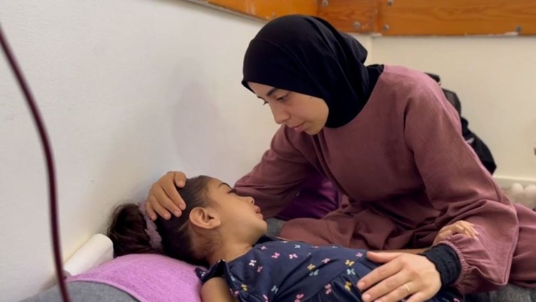 ガザの病院のマットレスに横たわり、母親に頭をなでてもらうヤスミンちゃん
/CNN