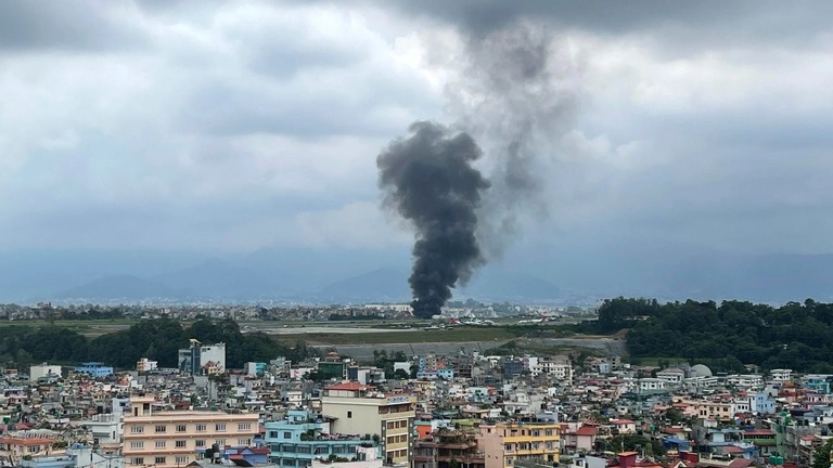 トリブバン国際空港で離陸直後に墜落した飛行機から立ち上る黒煙＝２４日、ネパール・カトマンズ/Agniia Galdanova/AP