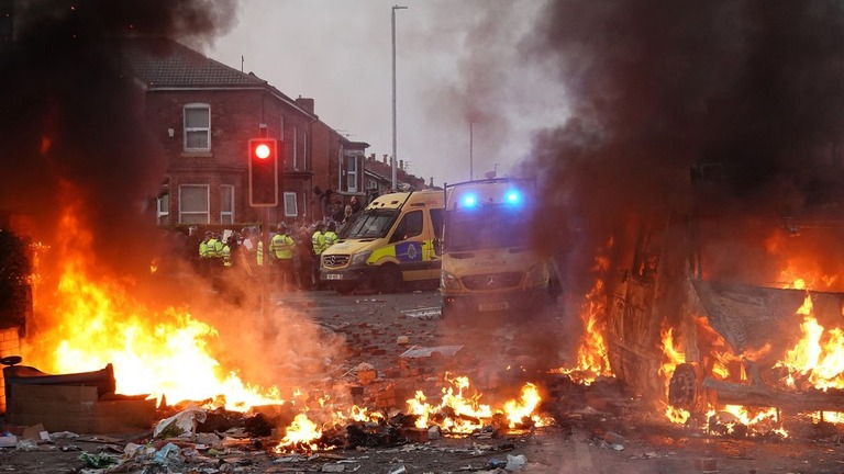 燃える警察車両の近くで暴徒を押し戻す警官隊＝英イングランド・サウスポート/Getty Images/Getty Images