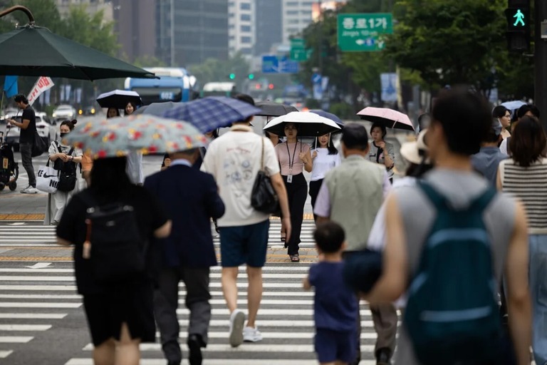 傘を手に道路を横断する歩行者。韓国の合計特殊出生率は０．７２と、世界最低水準にある＝８月５日、ソウル/SeongJoon Cho/Bloomberg/Getty Images