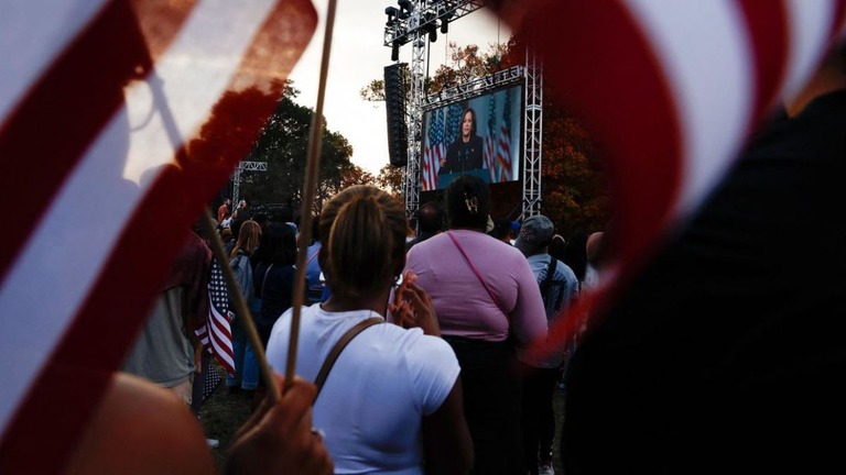 米大統領選での敗北を認める演説を行うカマラ・ハリス氏が映し出されたスクリーンを眺める支持者ら＝６日、米首都ワシントン/Evelyn Hockstein/Reuters