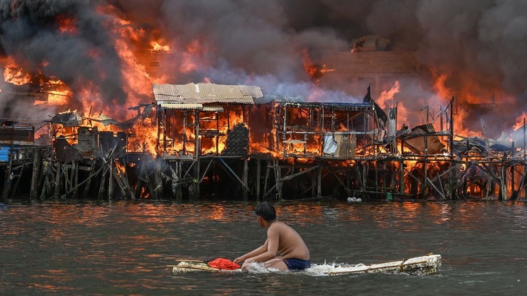 炎に包まれた家屋を眺める男性＝２４日、フィリピン・マニラ/Jam Sta Rosa/AFP/Getty Images