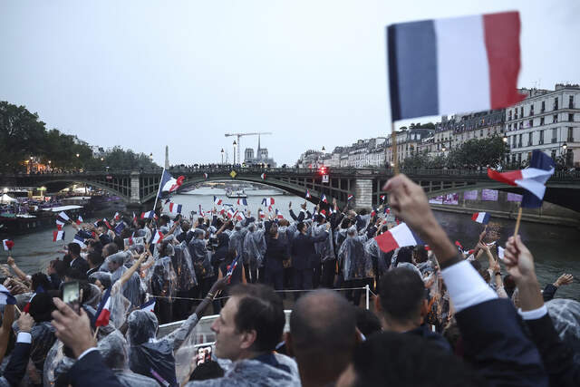 各国代表団がパレードでセーヌ川を下るなか、フランスの選手団が国旗を振っている。夏季五輪開会式が史上初めてスタジアムの外で行われた＝７月２６日、仏パリ/Franck Fife/Pool/AP