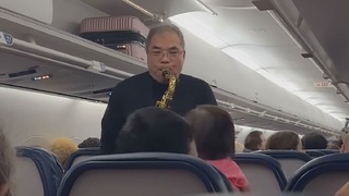 旅客機の機内でクリスマスソングを演奏するウェイン・ホーイさん