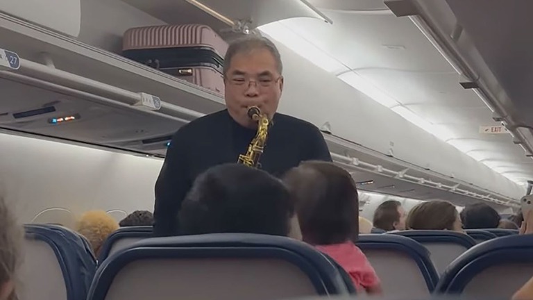 旅客機の機内でクリスマスソングを演奏するウェイン・ホーイさん/From Kate Dailey