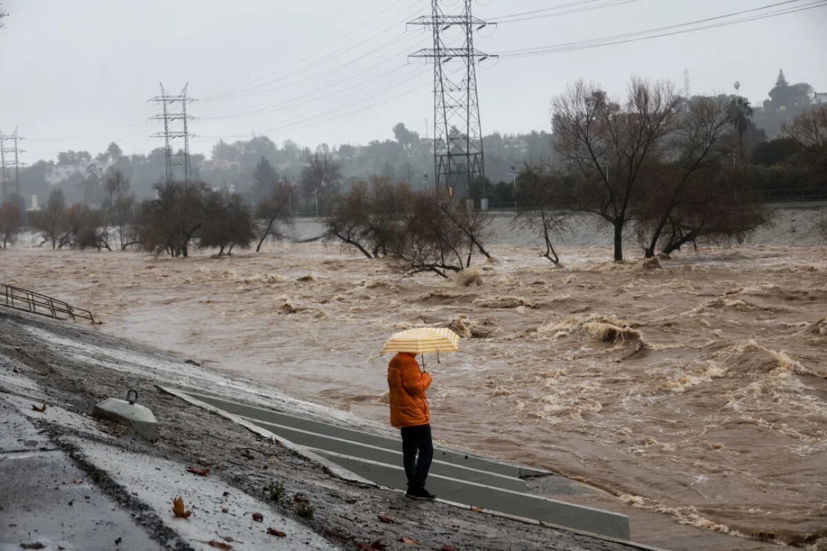 ロサンゼルスを襲った豪雨の中、傘を手にロサンゼルスの川を見つめる男性＝２４年２月５日/Aude Guerrucci/Reuters